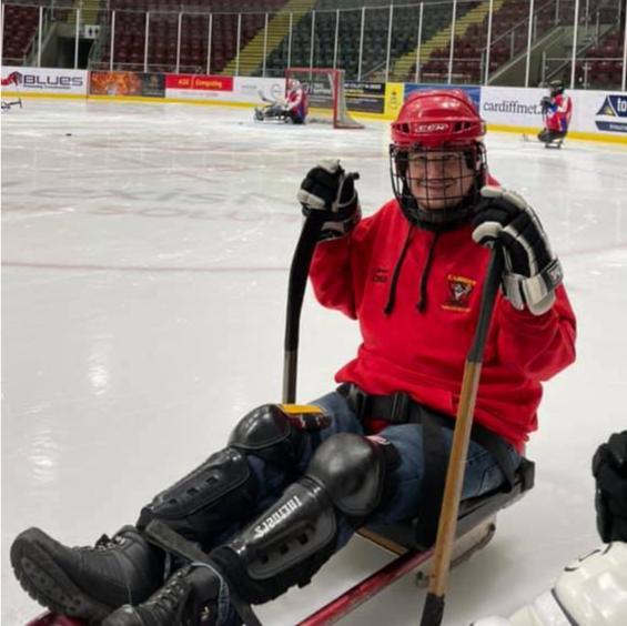 sat on a sledge, on ice at ice rink looking at the camera.